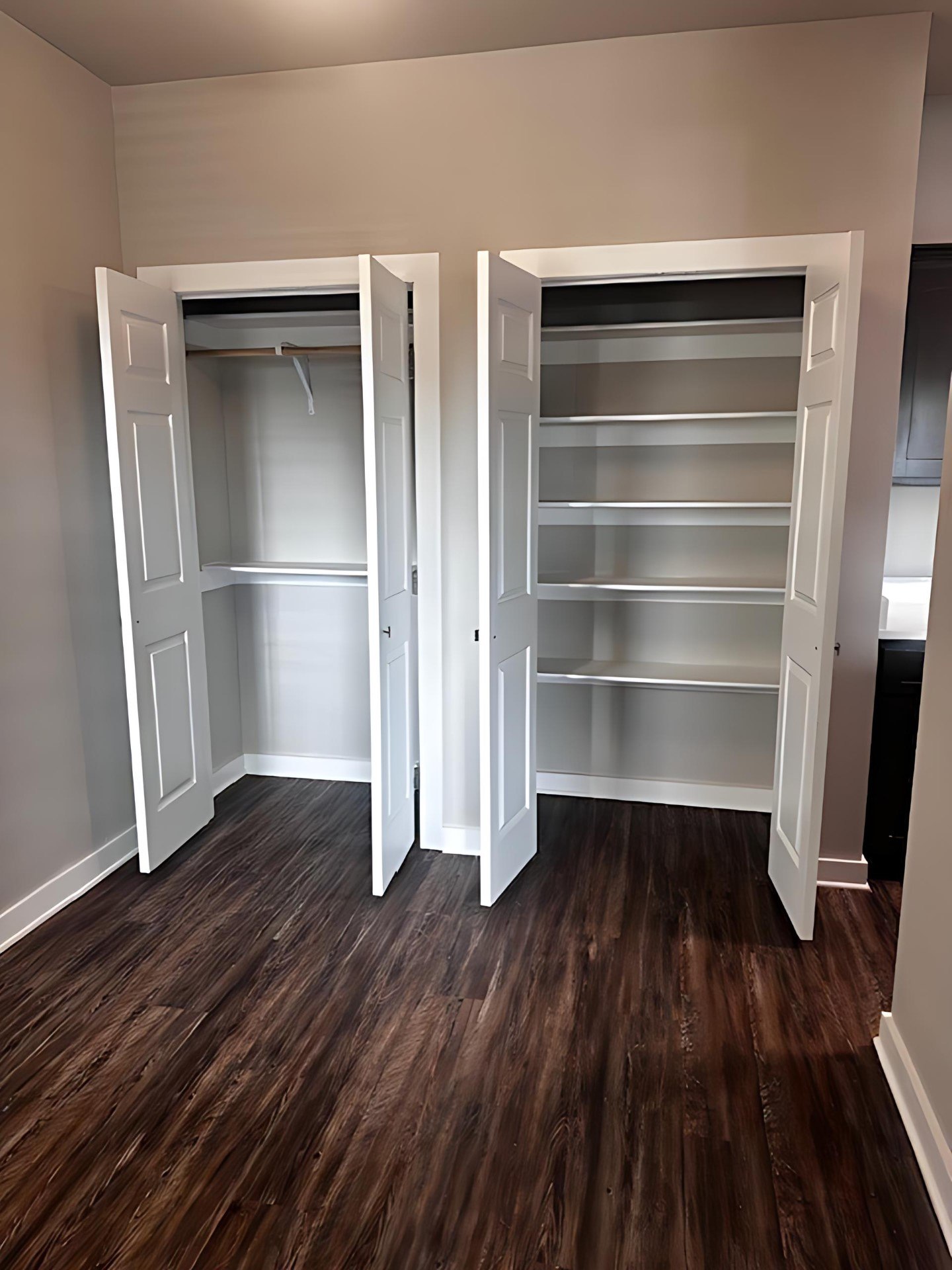 A room with two open closets and wood flooring.